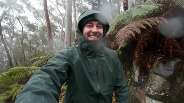 A man in a green waterproof jacket laughing in the rain on a misty bush track